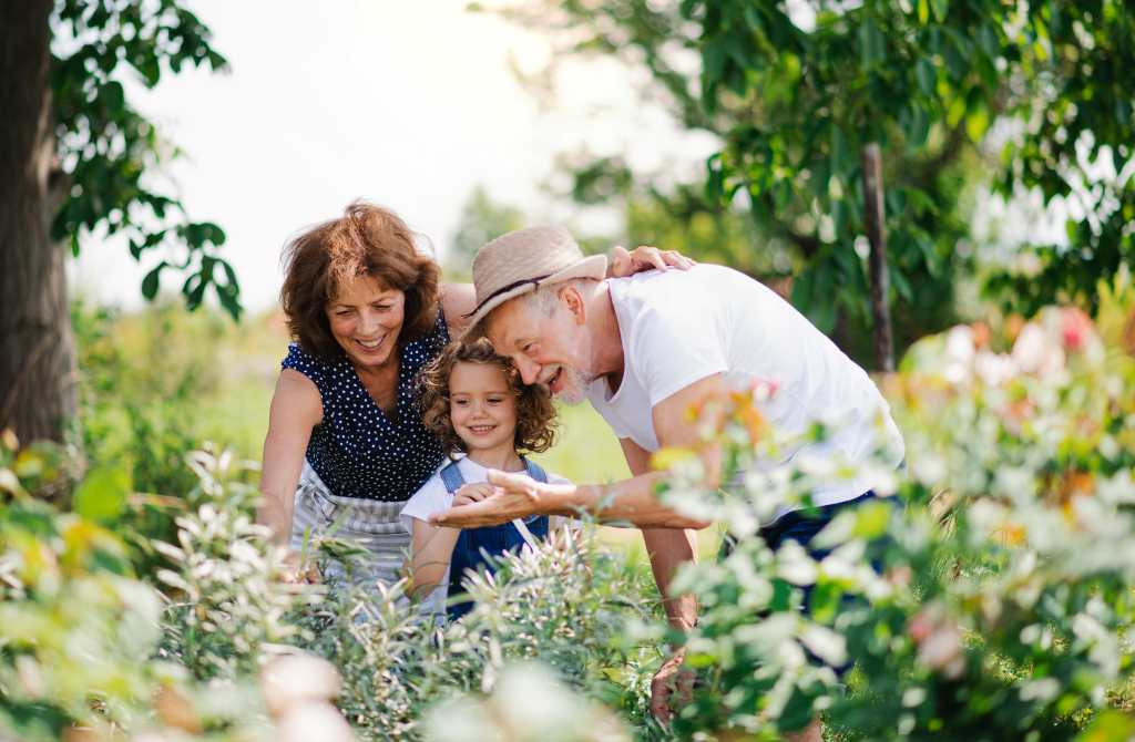 Grandparent, parent, and child standing together in a garden looking at flowers, representing family values and thoughtful estate planning.