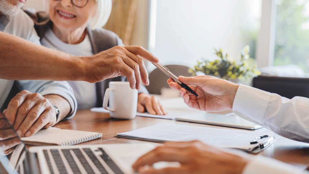 Hands writing with pens at a table beside coffee cups, representing thoughtful and customized estate planning.